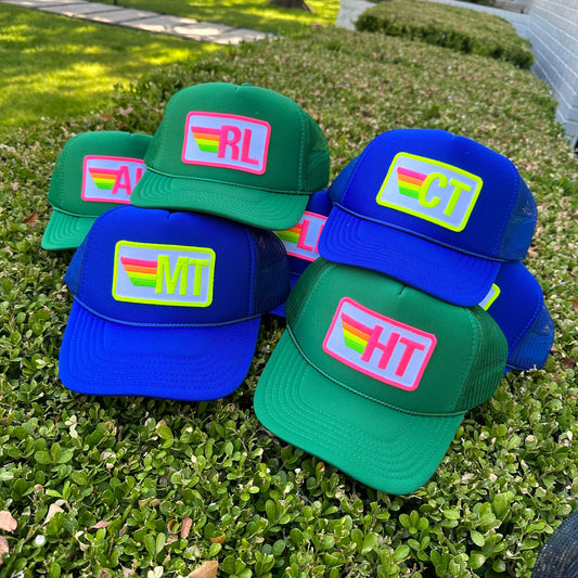 Green and blue trucker hats with retro rainbow-stripe monogram initial patches