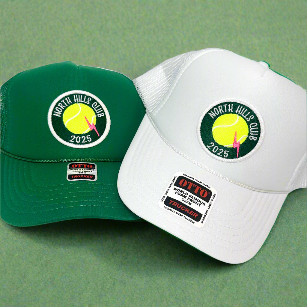 Two baseball caps, one green and one white, with 'North Hills Club 2025' logo on a light gray background.